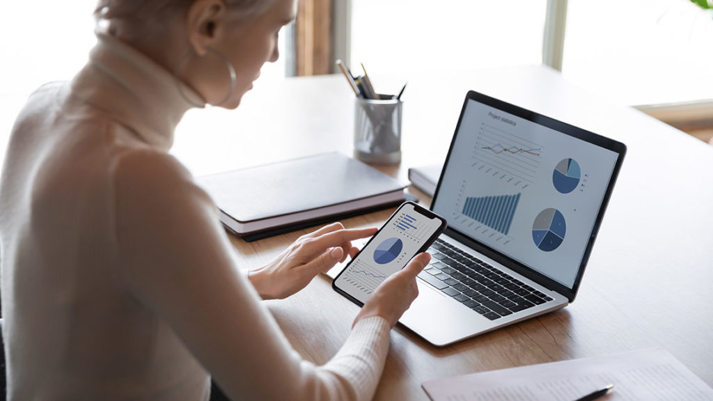 Rear view businesswoman holding smartphone, working with financial statistics